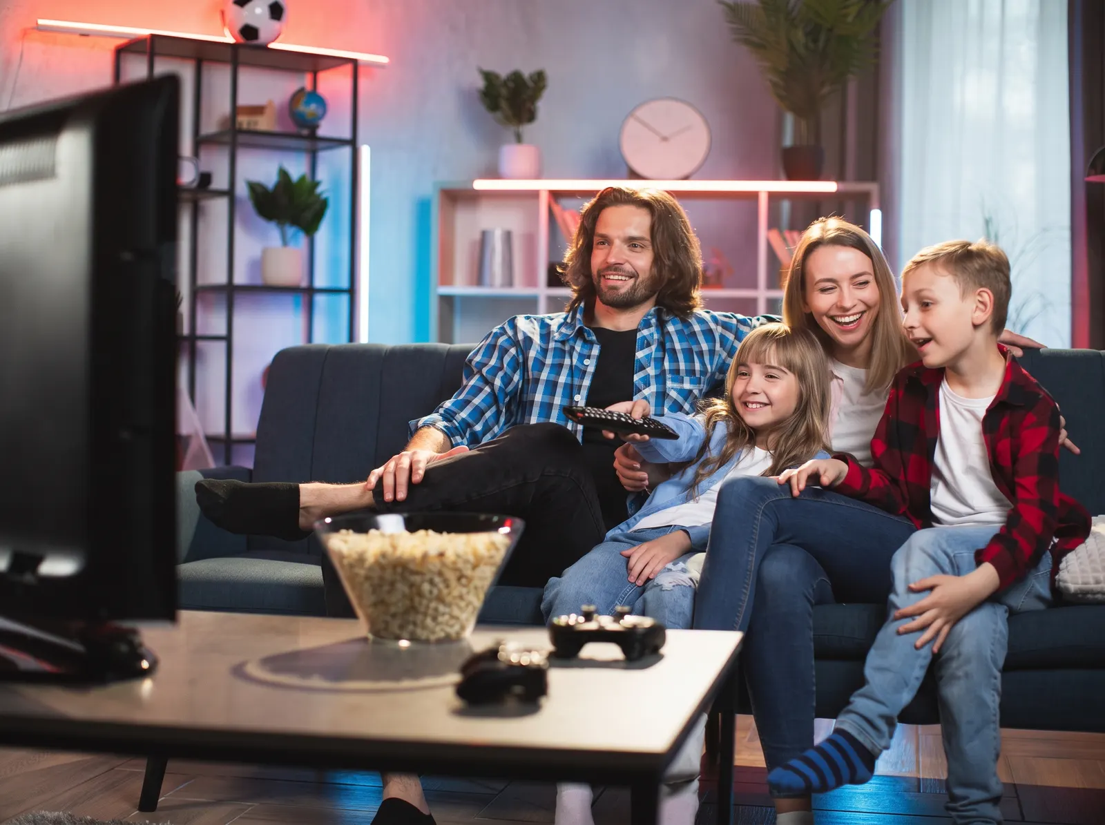Padres y dos niños riendo frente a la televisión con un tazón de palomitas